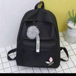 Tas ransel warna hitam dengan aksesoris pom pom warna abu bersandar di dinding