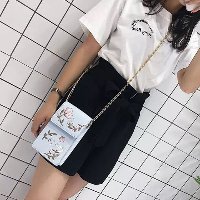 tas selempang warna biru muda dengan tali selempang rantai digunakan oleh wanita menggunakan kaos putih dan celana pendek hitam